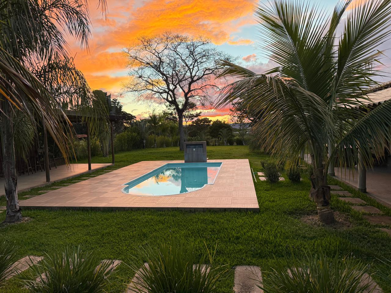 Piscina do Sítio Recanto do Sossego ao pôr do sol, cercada por gramado e coqueiros